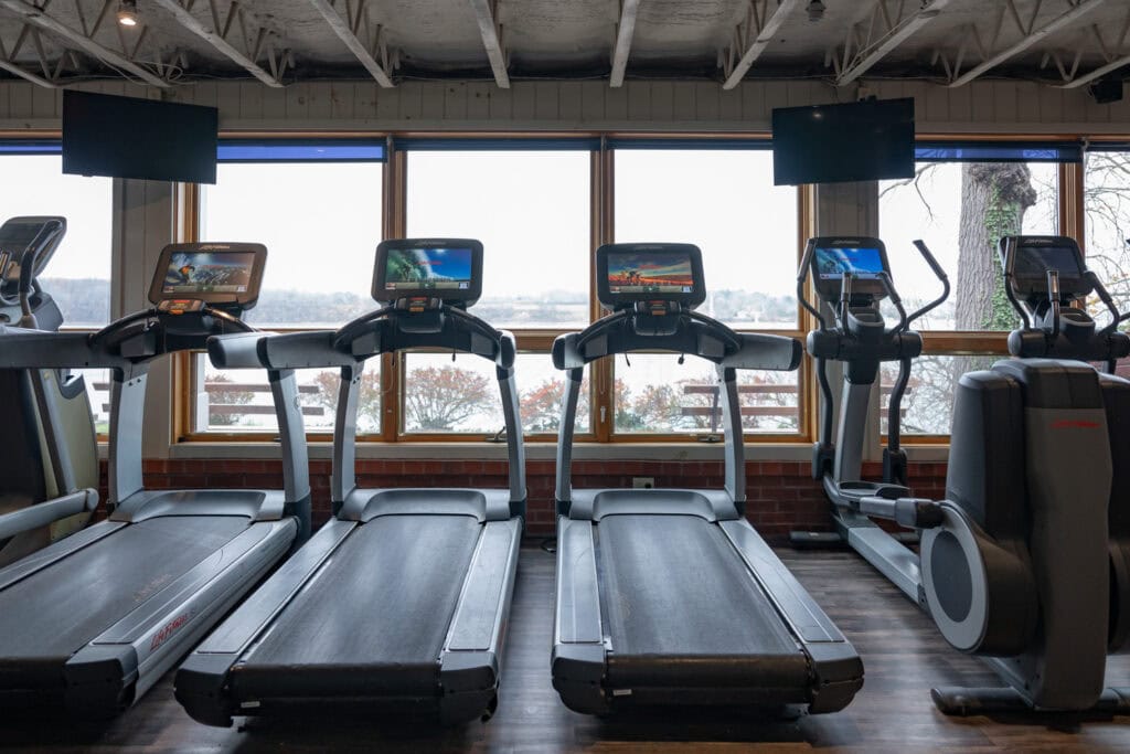 Row of treadmills with personal TV screens facing scenic windows at Apex Personal Fitness Youngstown NY