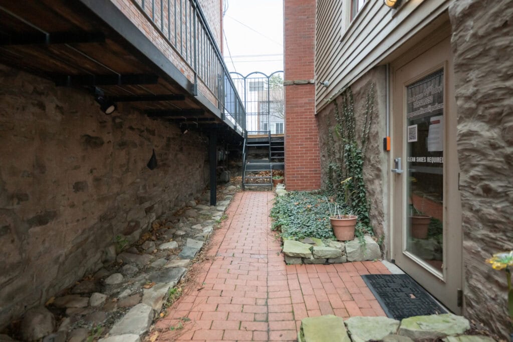 Wide brick pathway with plants and textured wall for outdoor fitness and wellness space.