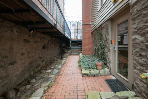 Wide brick pathway with plants and textured wall for outdoor fitness and wellness space.